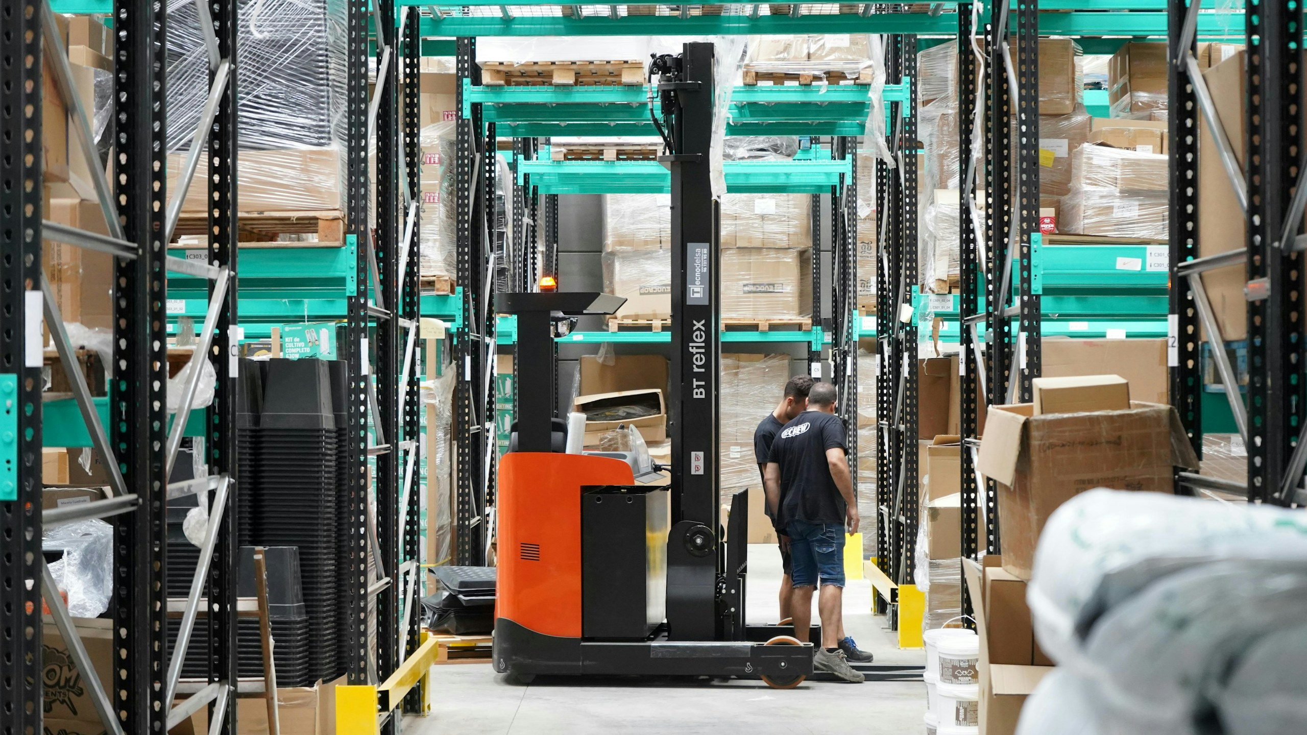 A worker checking cartons along a warehouse racking aisle